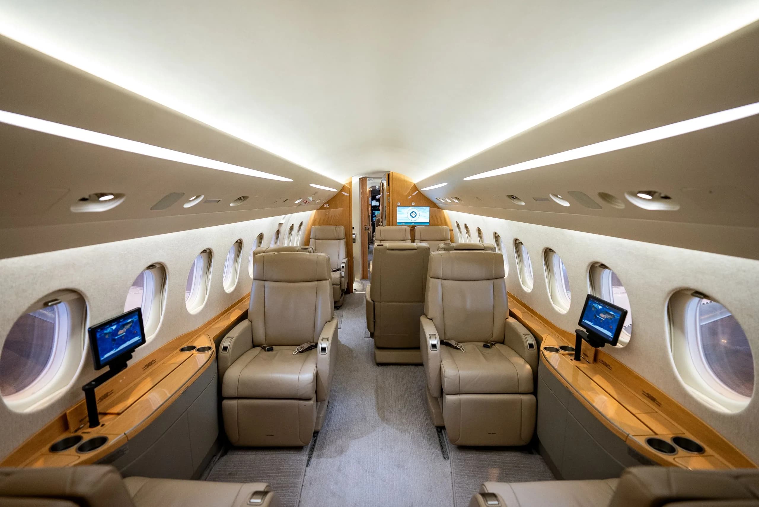 The luxurious interior cabin of a private jet, featuring tan leather seats and individual entertainment screens.