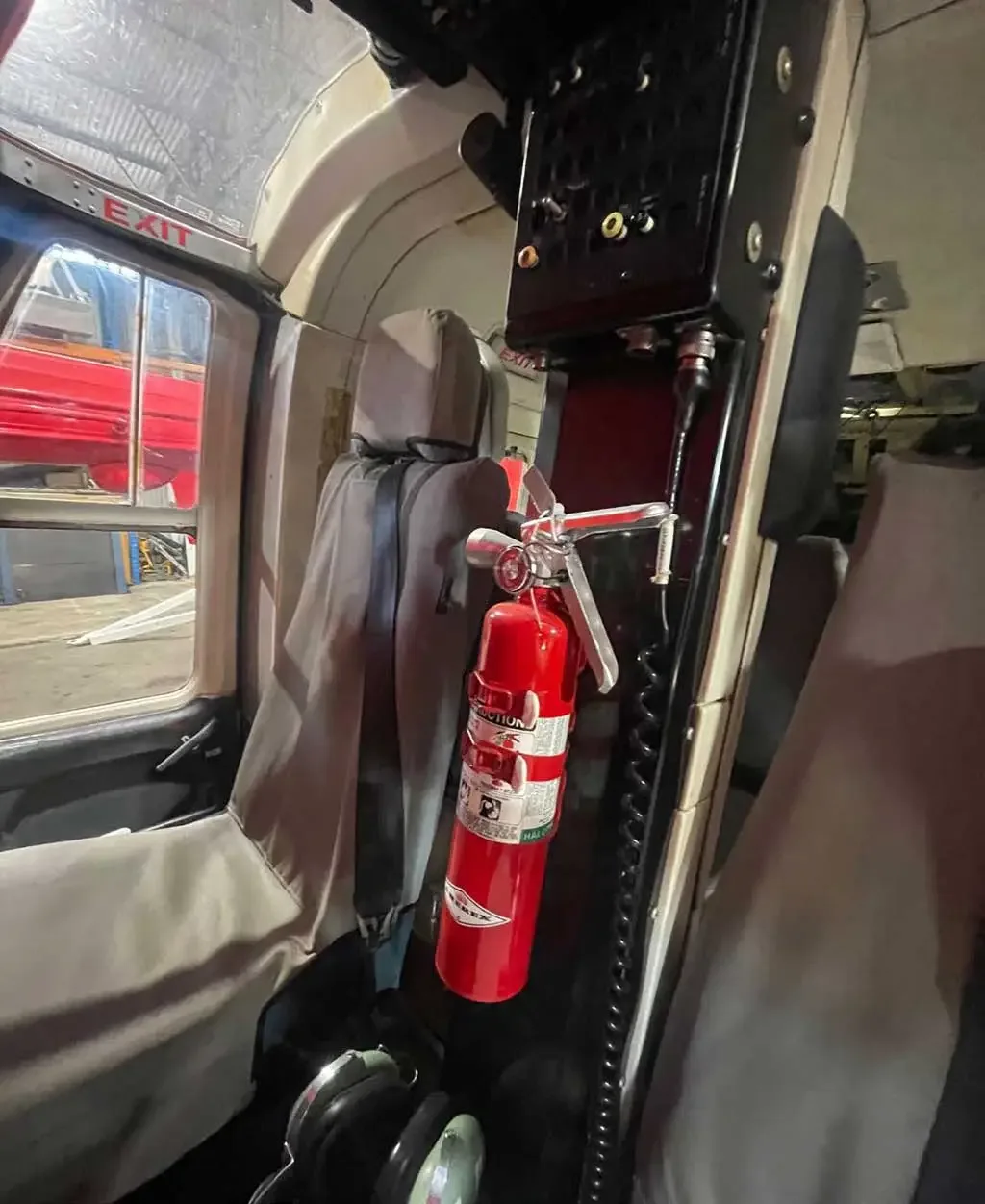 The interior of a helicopter cabin showing a red fire extinguisher mounted near the passenger seats.
