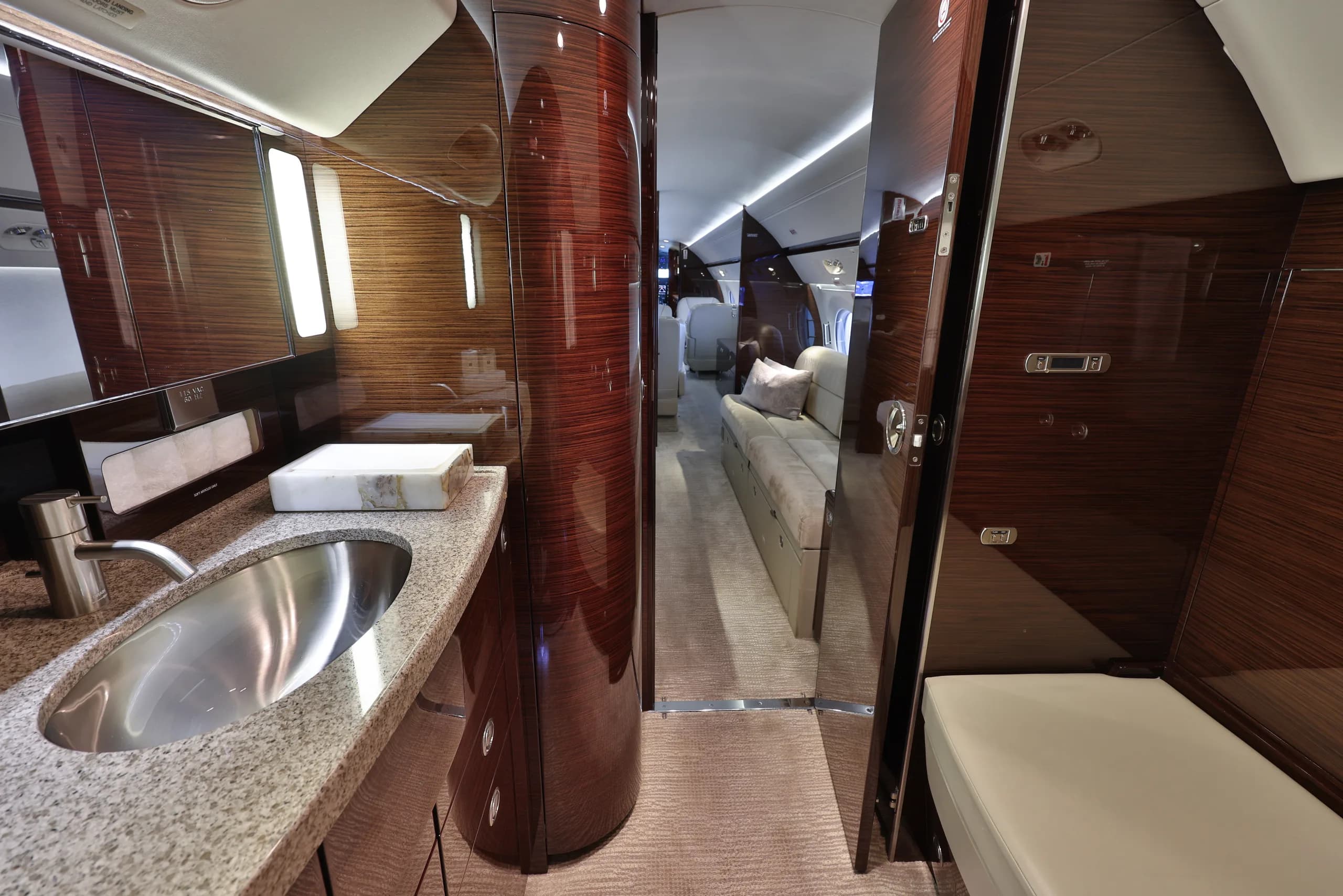 A luxurious aircraft lavatory with a granite counter and sink, looking into the main cabin.