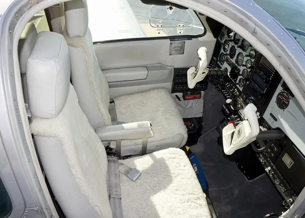 The cockpit of a Beechcraft Baron 58 features light gray seats with white sheepskin covers and dual yokes.