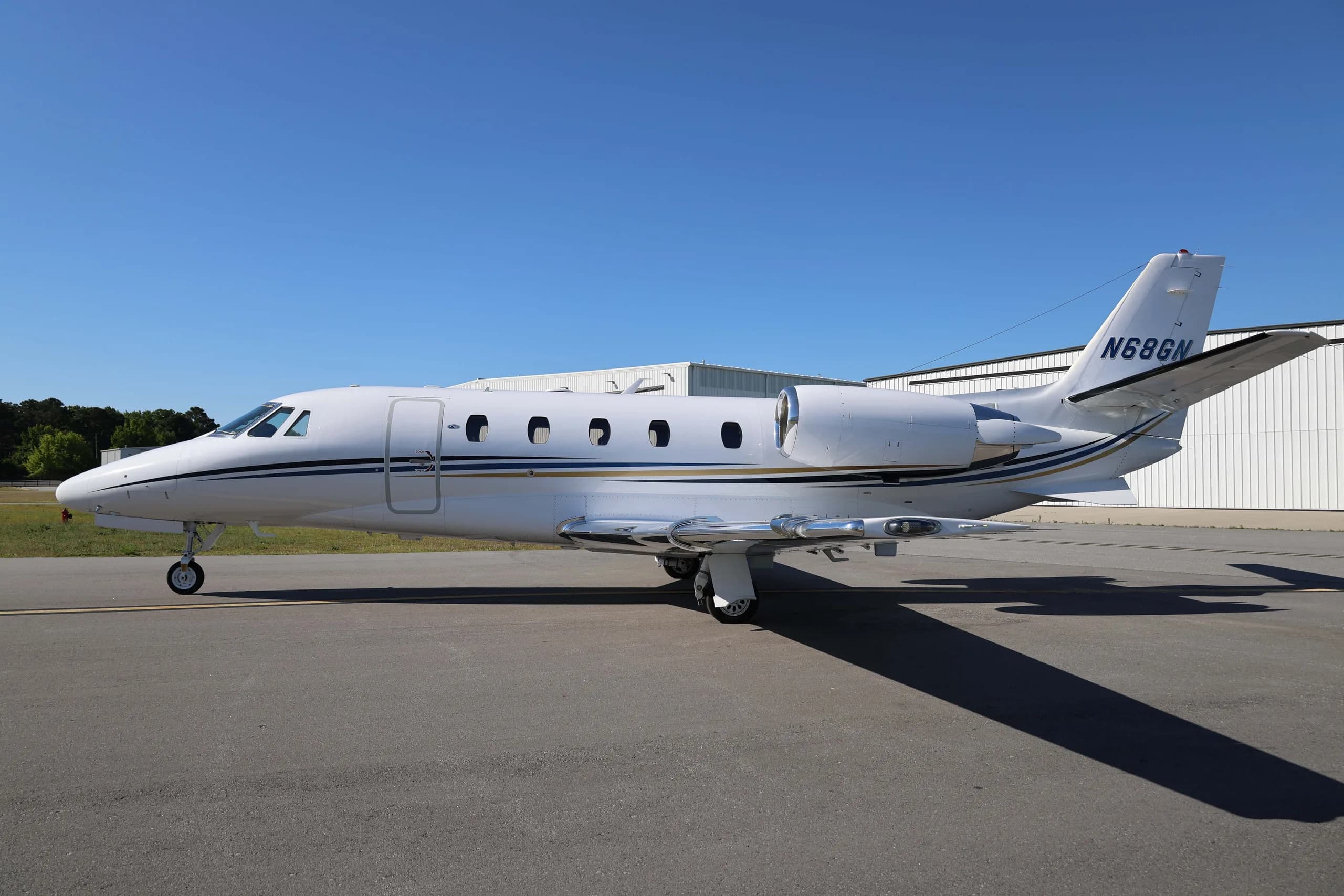 A side view of the white Cessna Citation business jet N68GN with black and gold stripes.