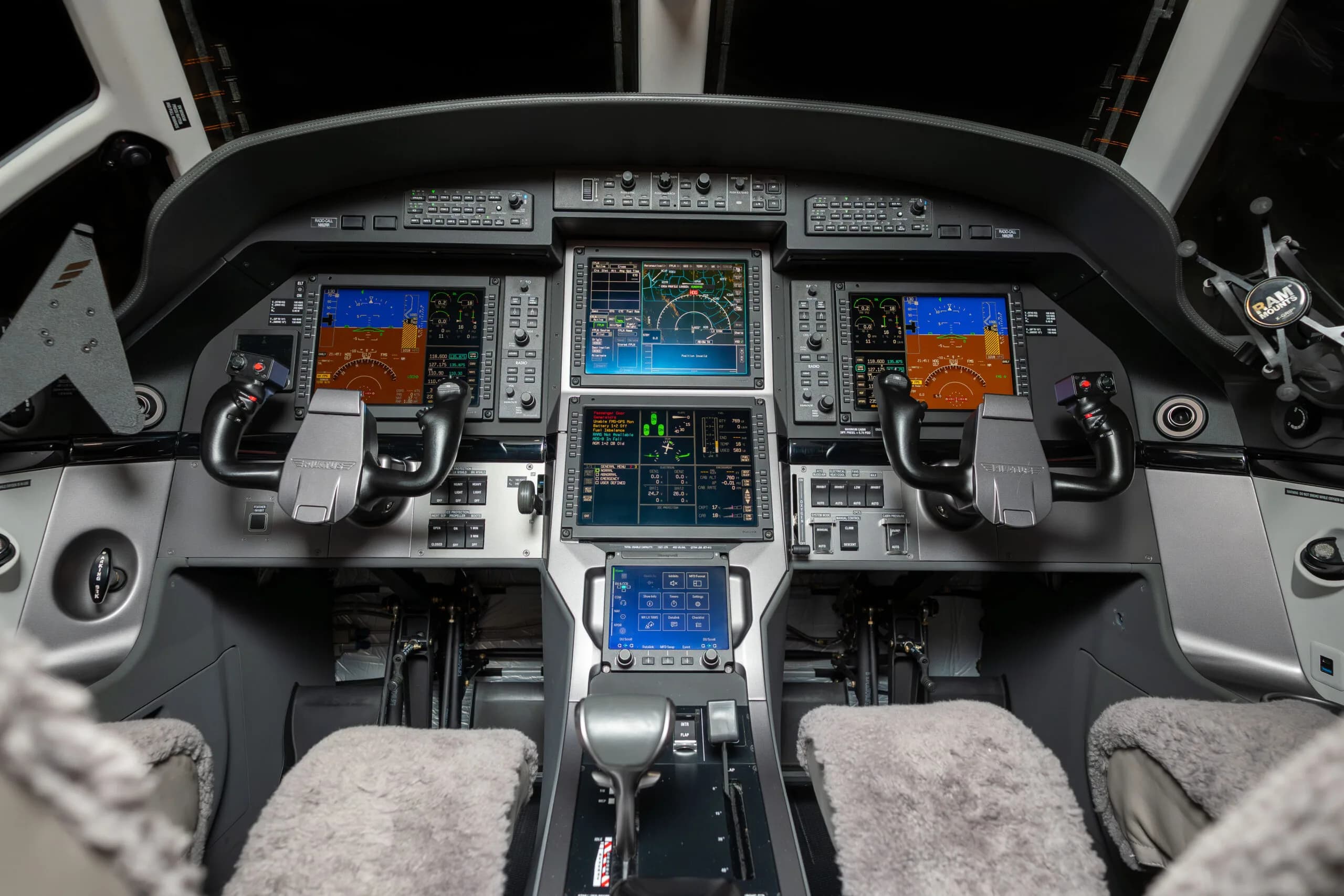 The modern glass cockpit of a Pilatus PC-12 aircraft, featuring multiple large display screens and control yokes.