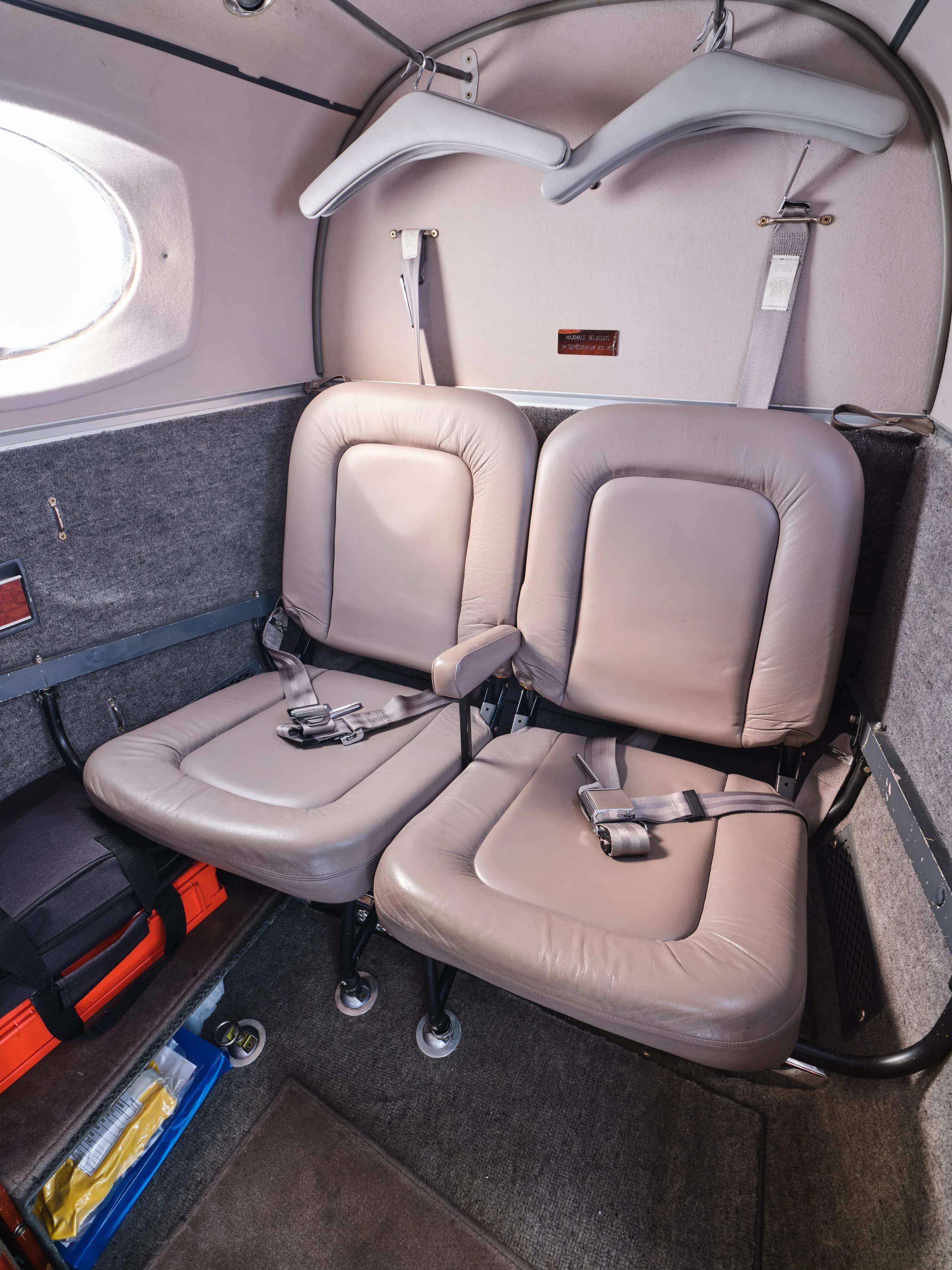 Two light brown leather utility seats are visible in a rear section of the aircraft cabin, with a window on the left.