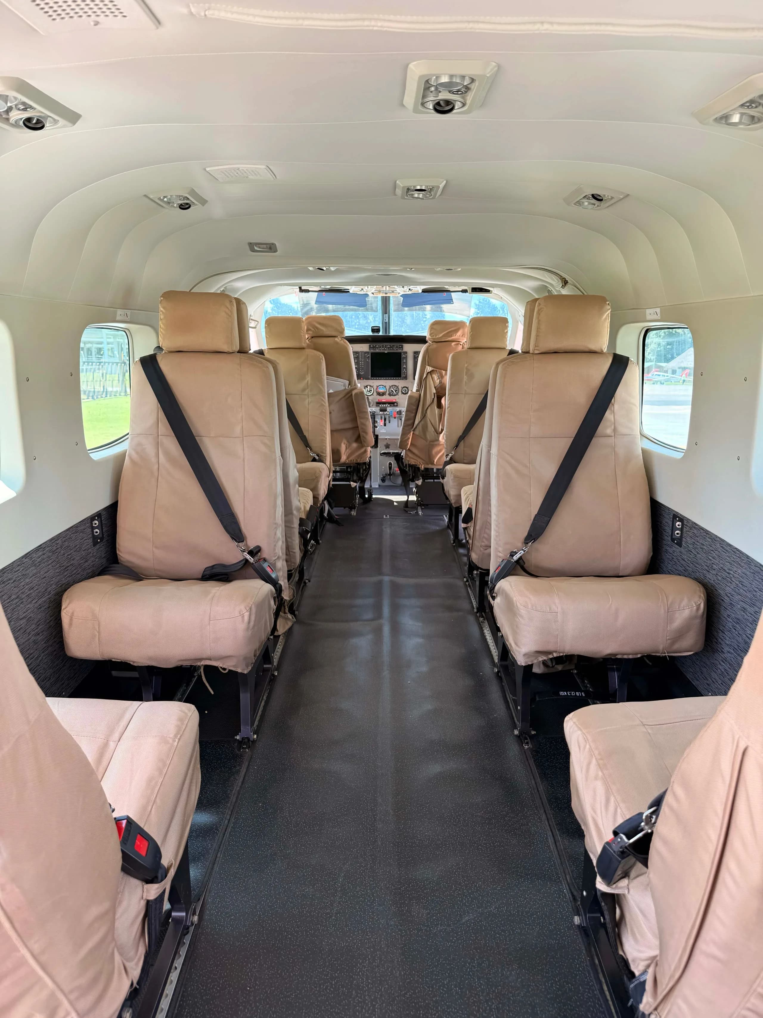 The interior cabin of an aircraft with tan fabric seats leading to the cockpit.
