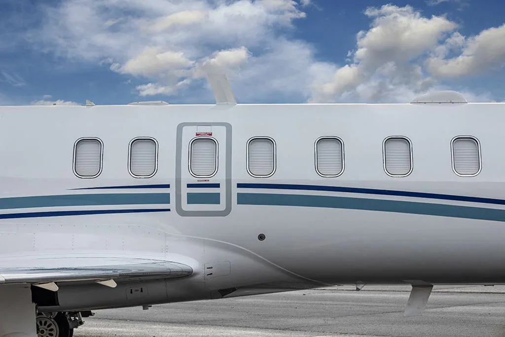 Close-up of the white fuselage of a business jet with a blue stripe, showing windows and the main entry door.