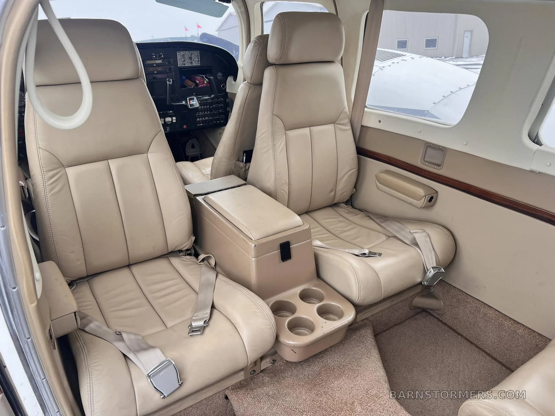 The tan leather interior cabin of a small aircraft, showing two rows of seats and a center console with cup holders.