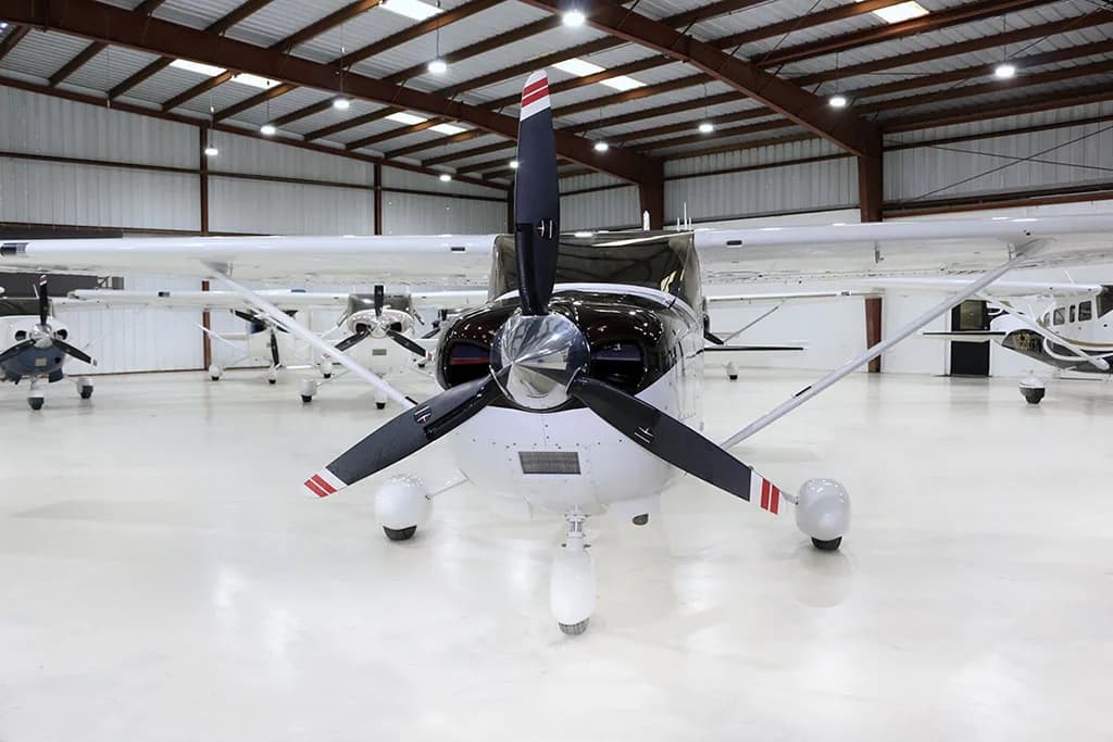A white and black Cessna Skylane N865JP with brown accents is parked head-on in a hangar.
