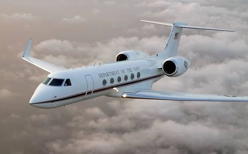 A Gulfstream G-V aircraft with 'Department of the Navy' livery flying through the clouds.