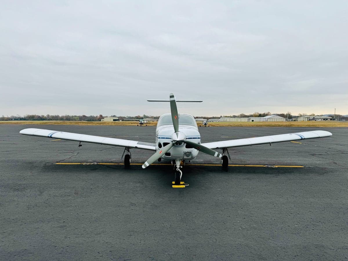 Front view of a white single-engine propeller aircraft with blue stripes parked on an airfield.