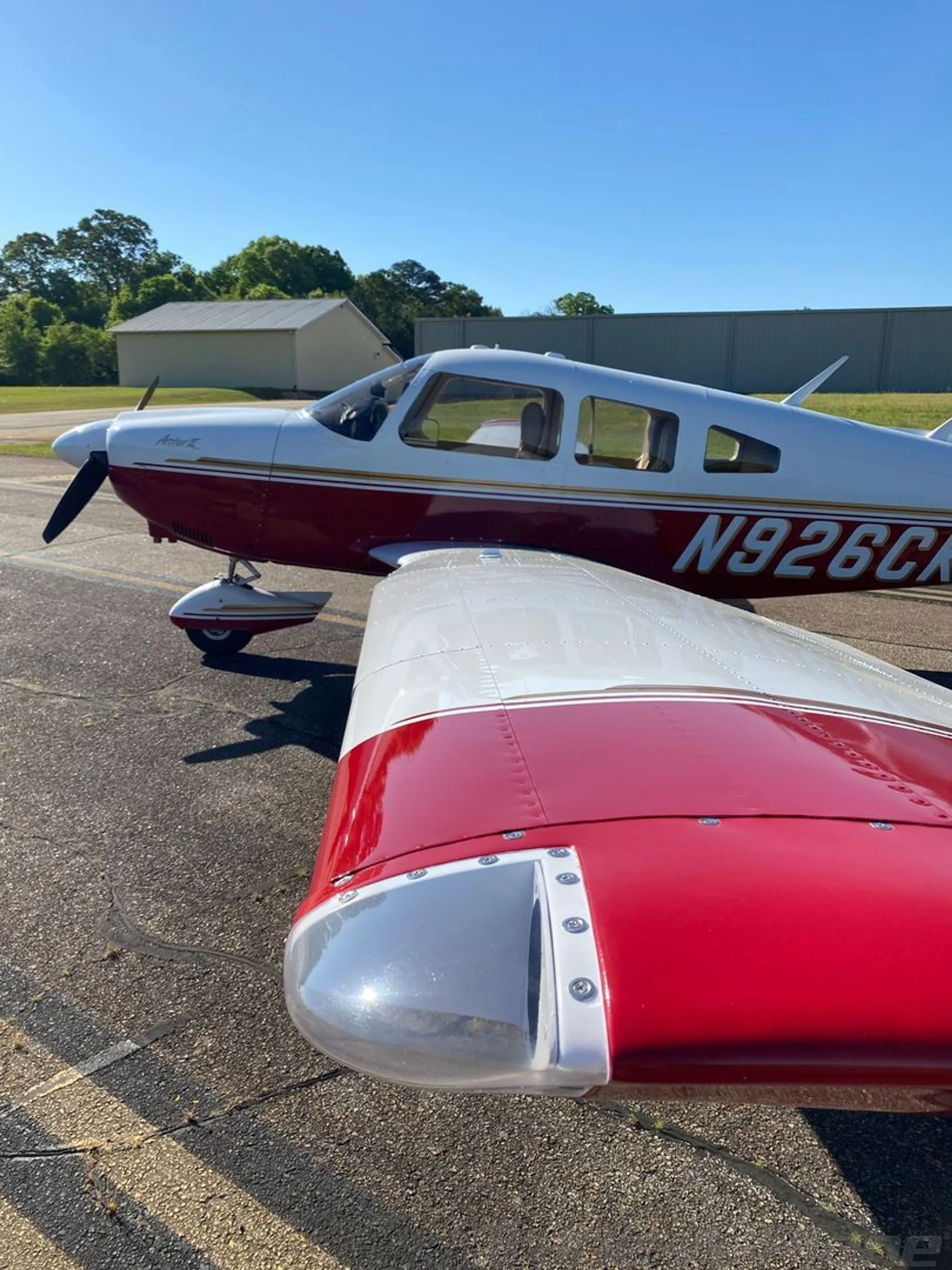 A close-up view of the right wing and fuselage of a white and red Piper Arrow II (N926CK) on the tarmac.