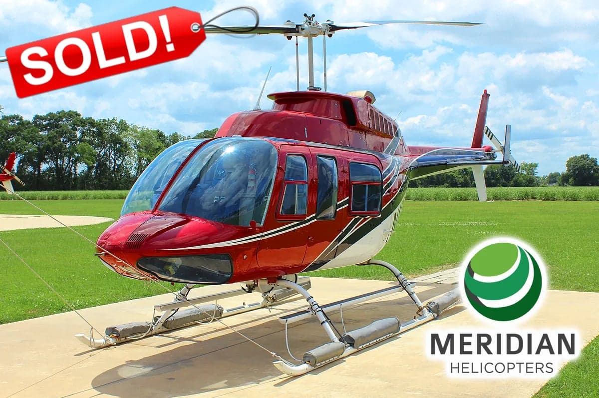 A red and white Bell 206 helicopter is parked on a concrete pad with a 'SOLD!' tag overlay.