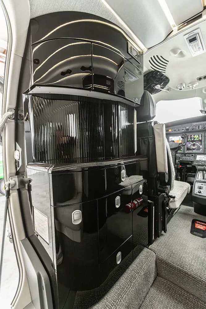 A vertical shot of the private jet's galley or storage area, featuring glossy black cabinets and a glimpse of the cockpit.