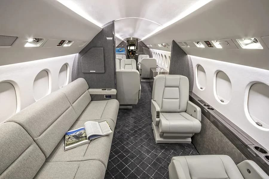 A long view of the private jet's elegant cabin with a grey sofa, individual seats, and a dark patterned aisle.