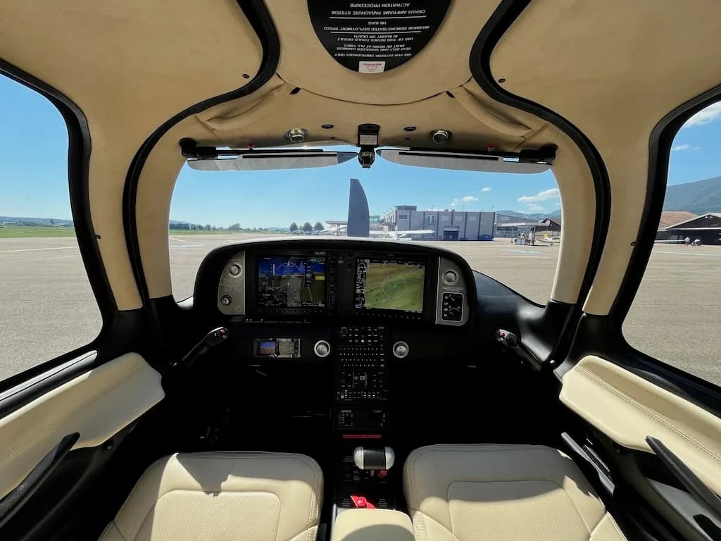 View from the cockpit showing the instrument panel with multiple screens and the airfield outside the windshield.