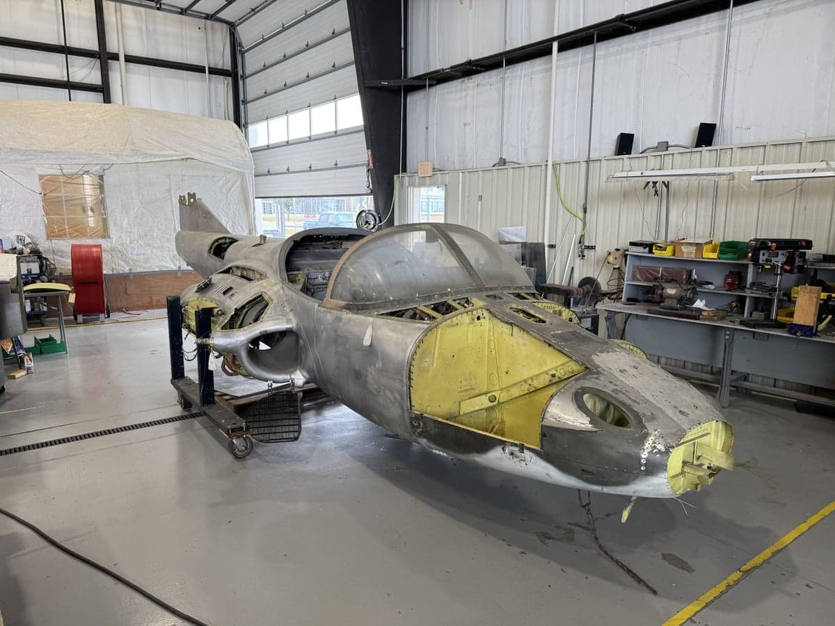 The front section of an aircraft undergoing restoration in a hangar.