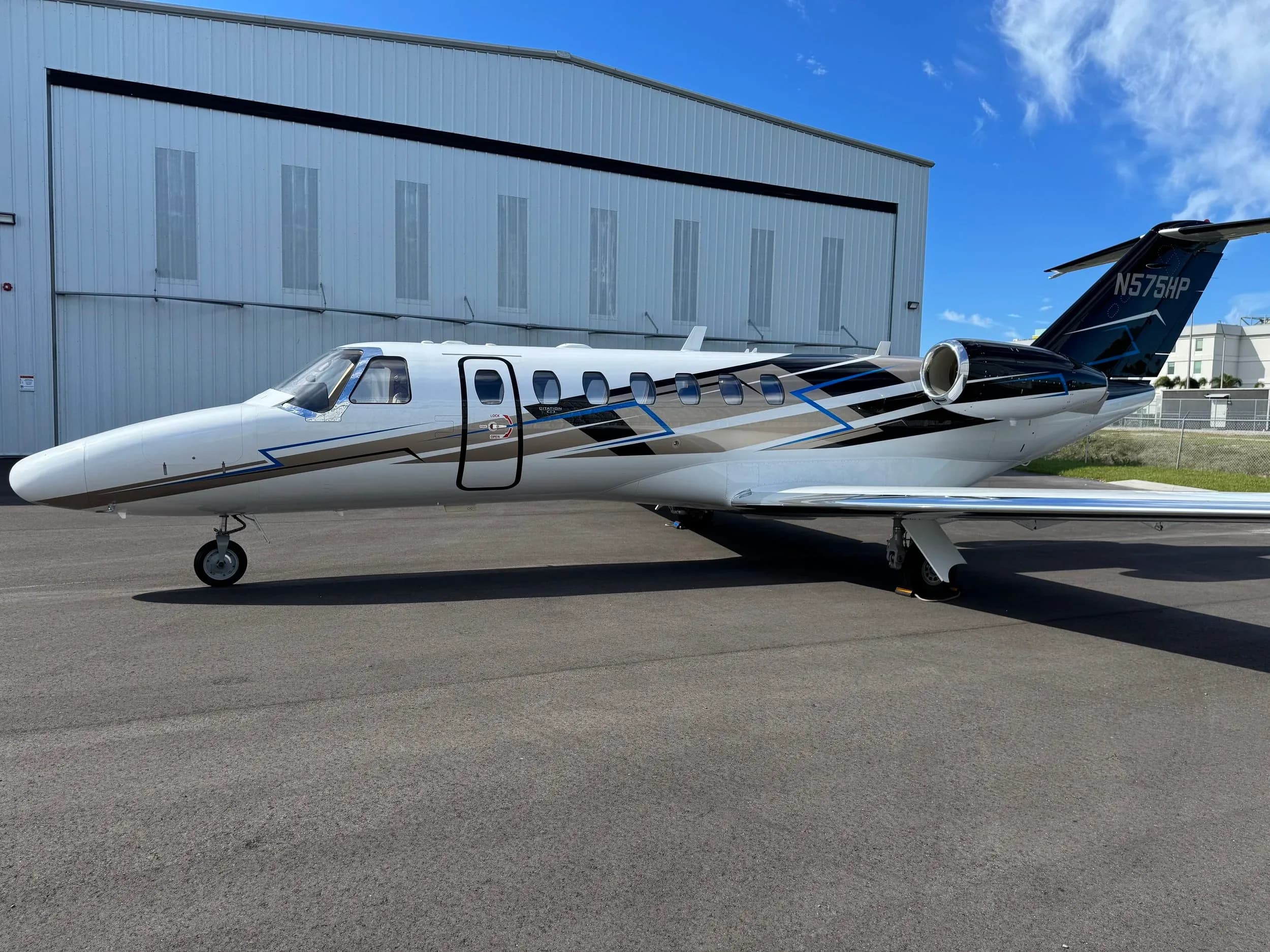 A Citation jet with a white and black paint scheme is parked in front of a hangar.