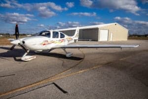 A Cirrus SR22 aircraft with a custom paint scheme is parked on the tarmac in front of a hangar.
