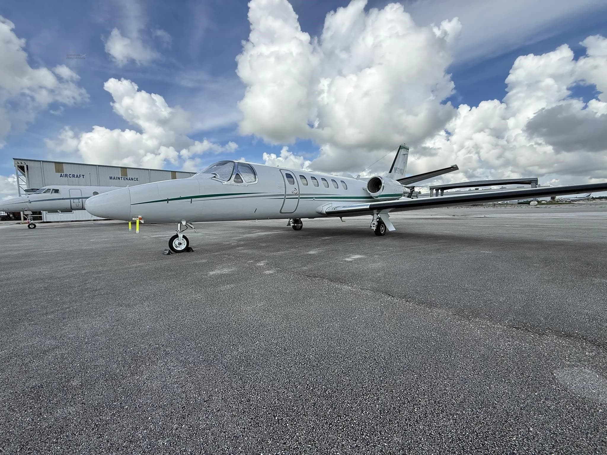 A white business jet with green stripes, registration N524XA, parked on an airport tarmac with a hangar in the background.