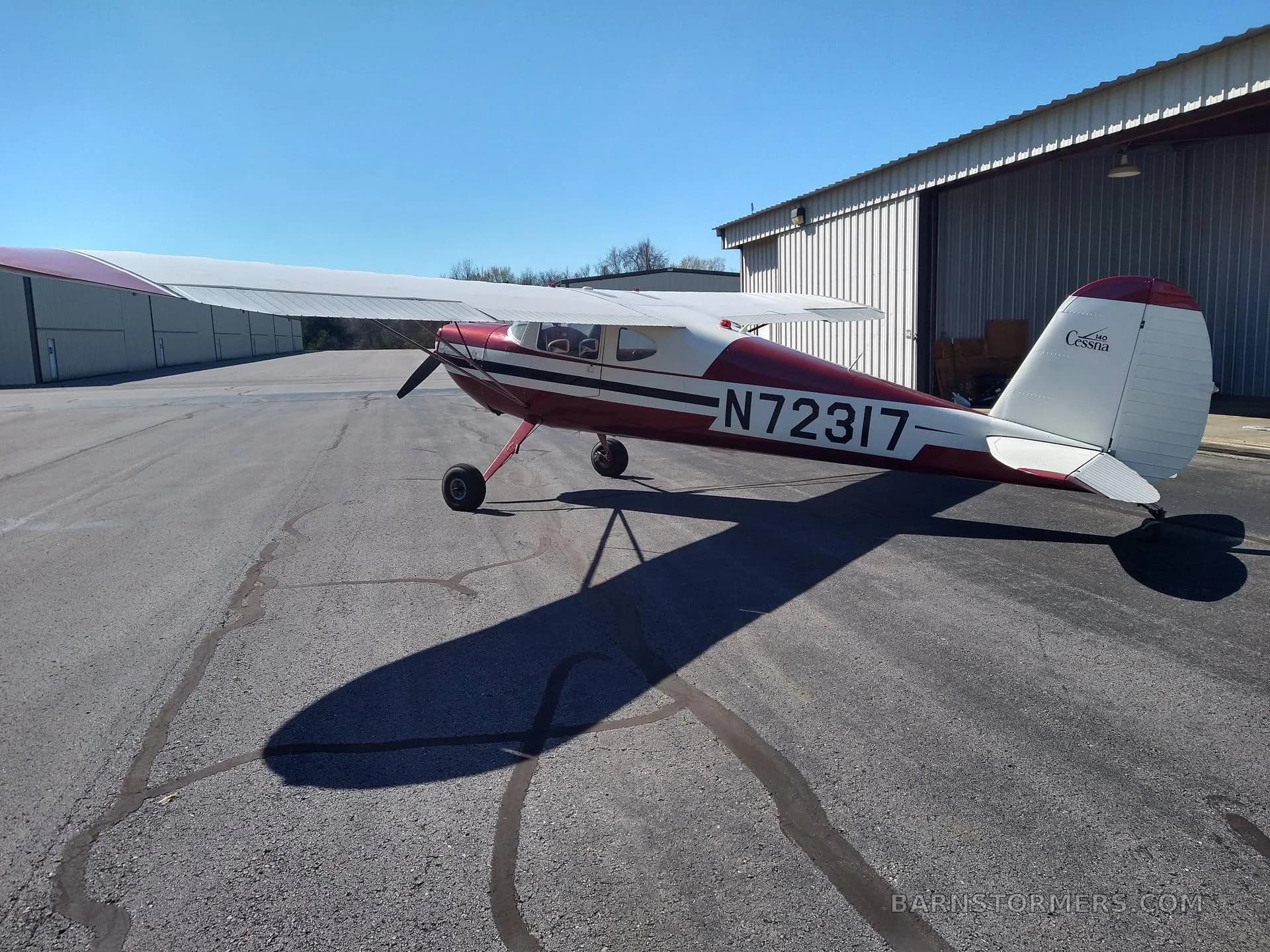 A three-quarter rear view of a red and white Cessna 140 aircraft (N72317) parked on an asphalt tarmac.