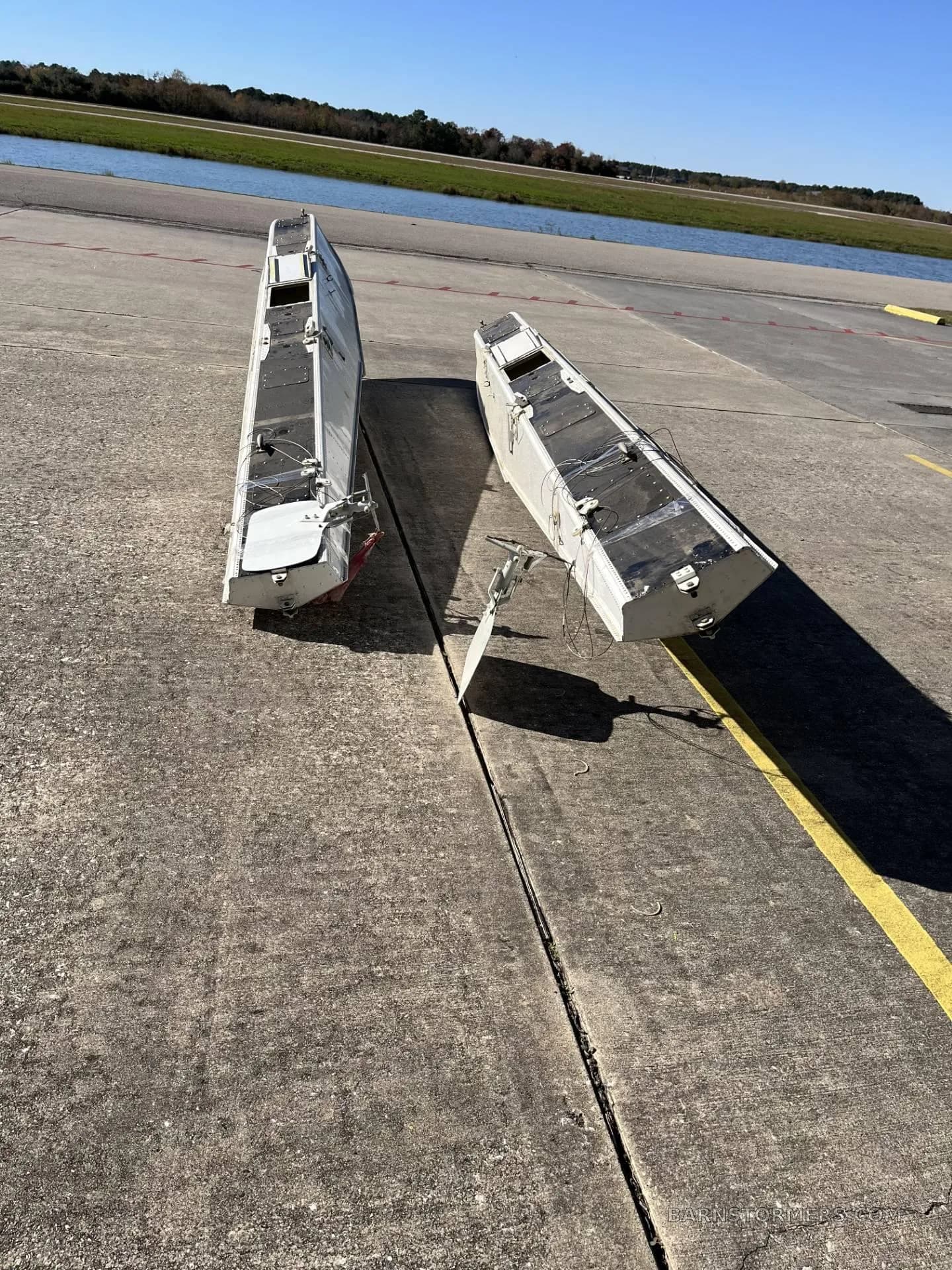 Two white aircraft floats with black tips lying on a concrete runway or taxiway.
