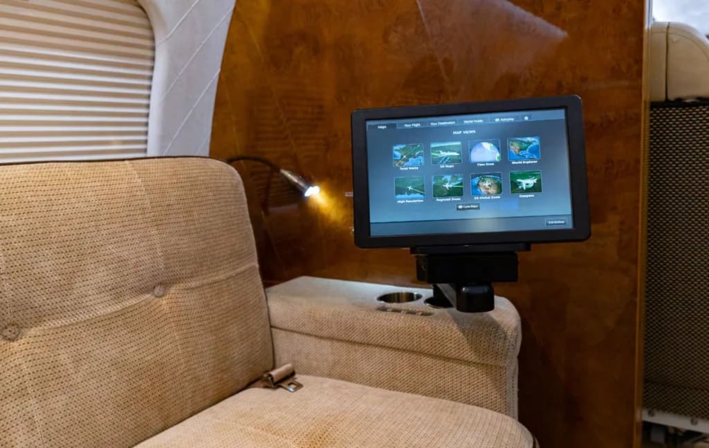 A close-up of an in-flight entertainment screen displaying map views, mounted next to a beige aircraft seat.