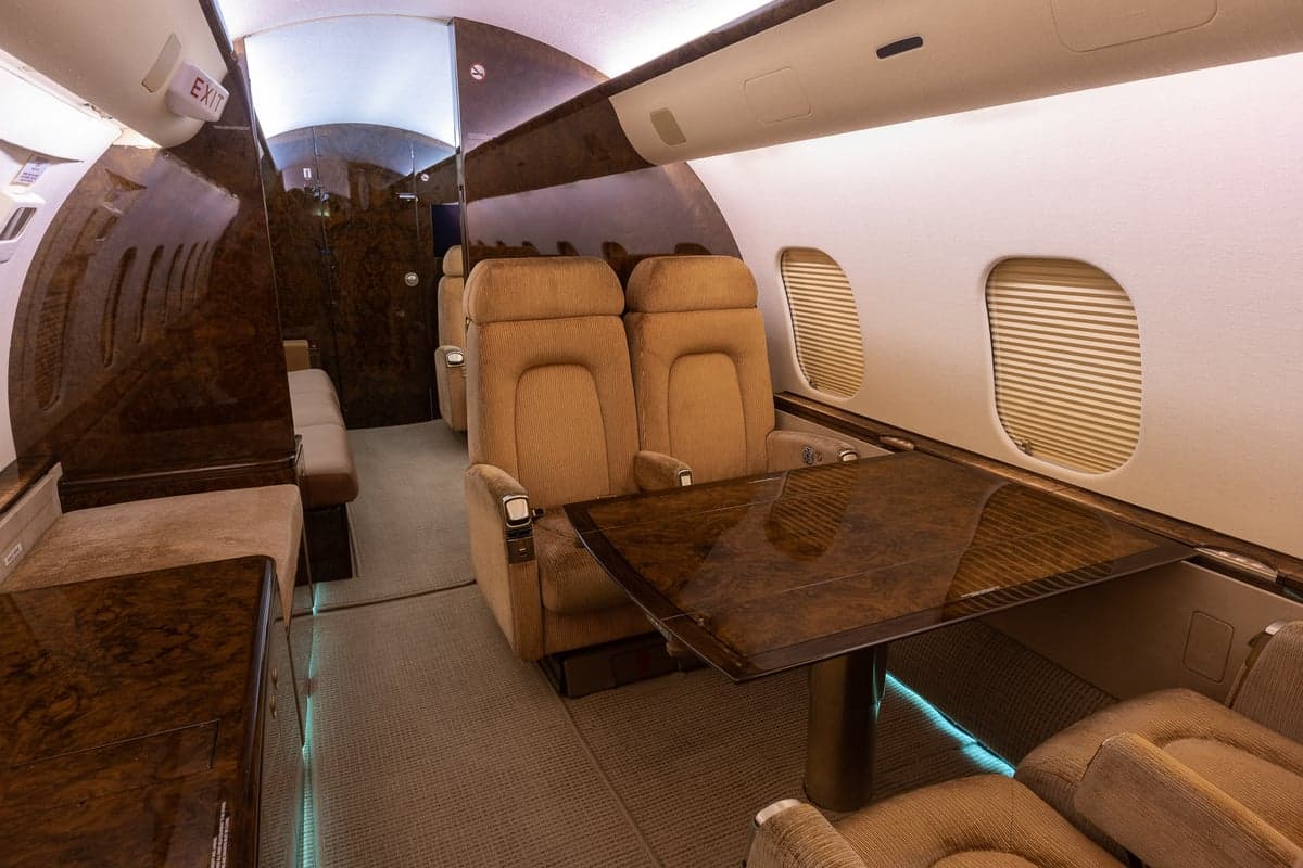 The interior of a Bombardier Global Express aircraft with tan leather seats, a table, and wood trim.