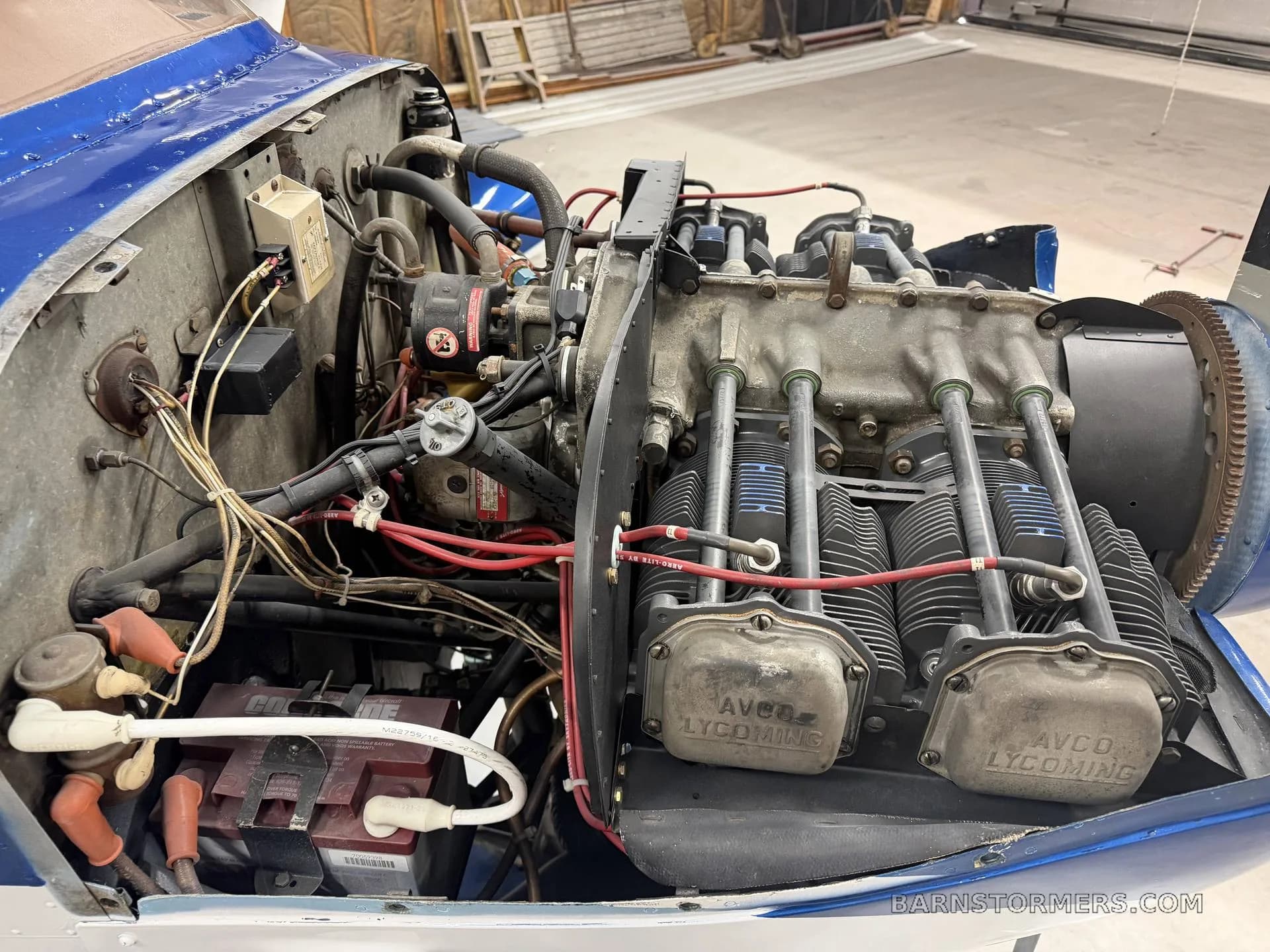 The open engine bay of a blue and white aircraft reveals an Avco Lycoming engine.