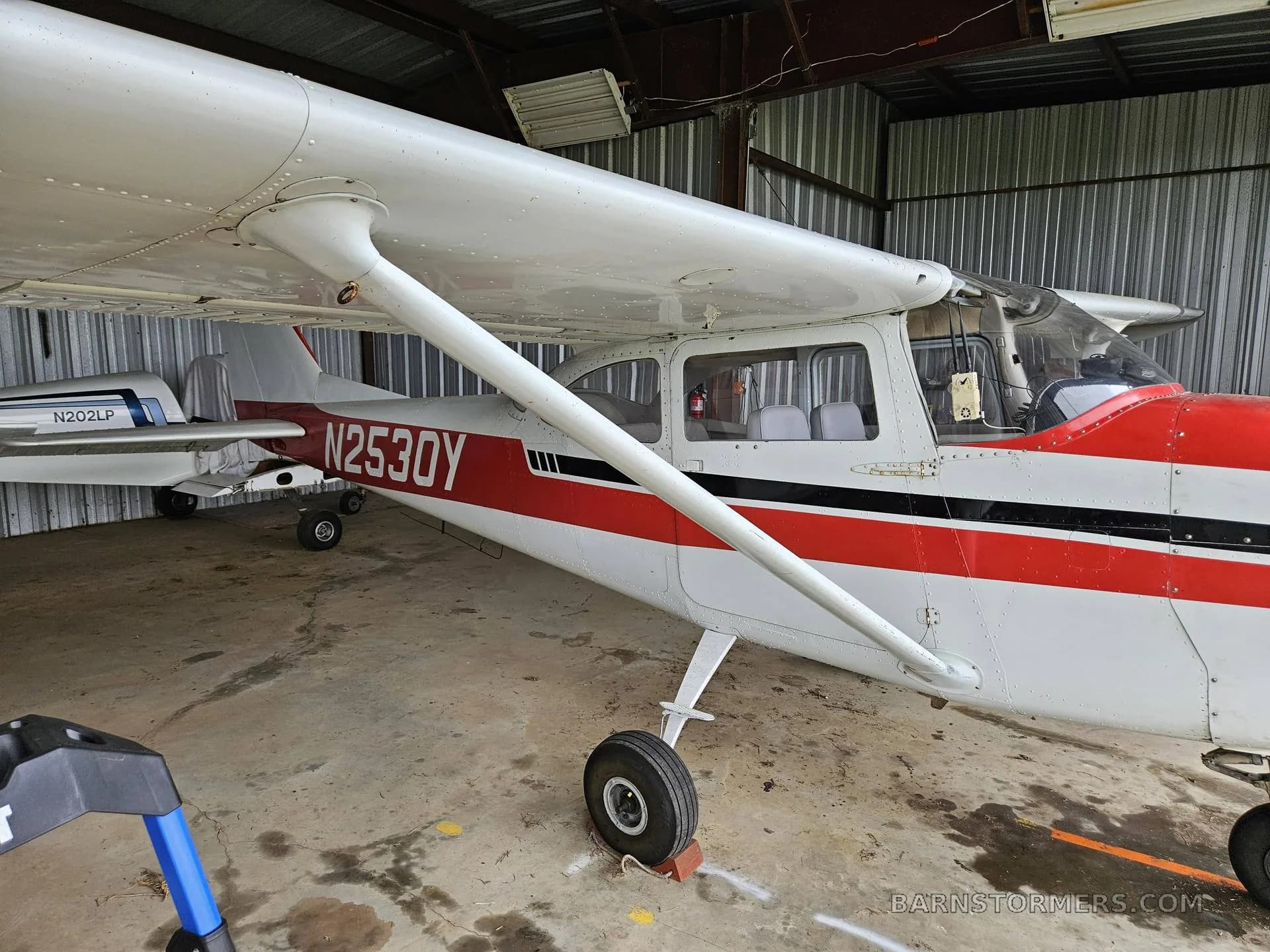 A three-quarter front view of a white and red single-engine propeller aircraft, N2530Y, parked inside a metal hangar.