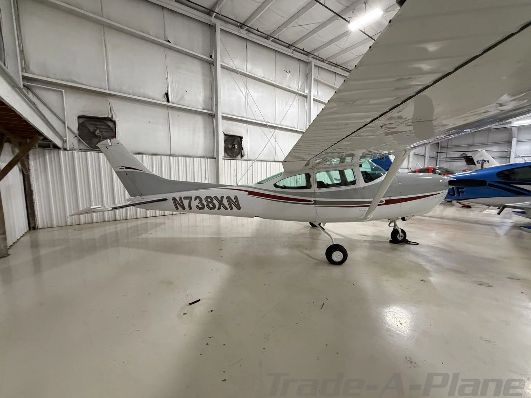 A side view of a white and grey Cessna 182 with red accents and N738XN registration, parked in a hangar.