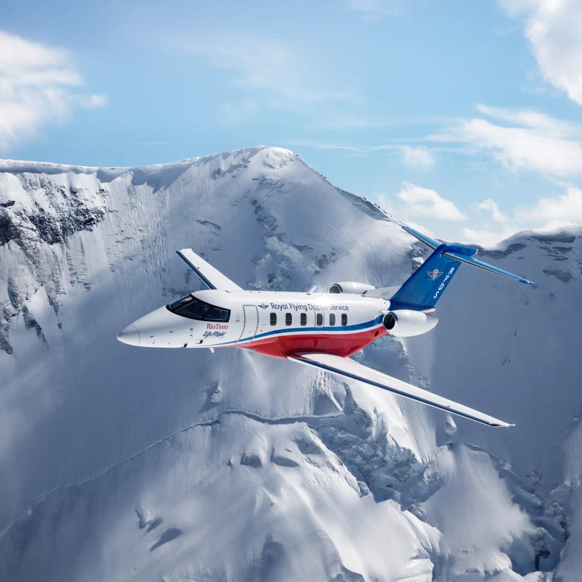 A Pilatus PC-24 aircraft in flight over a snowy mountain range.