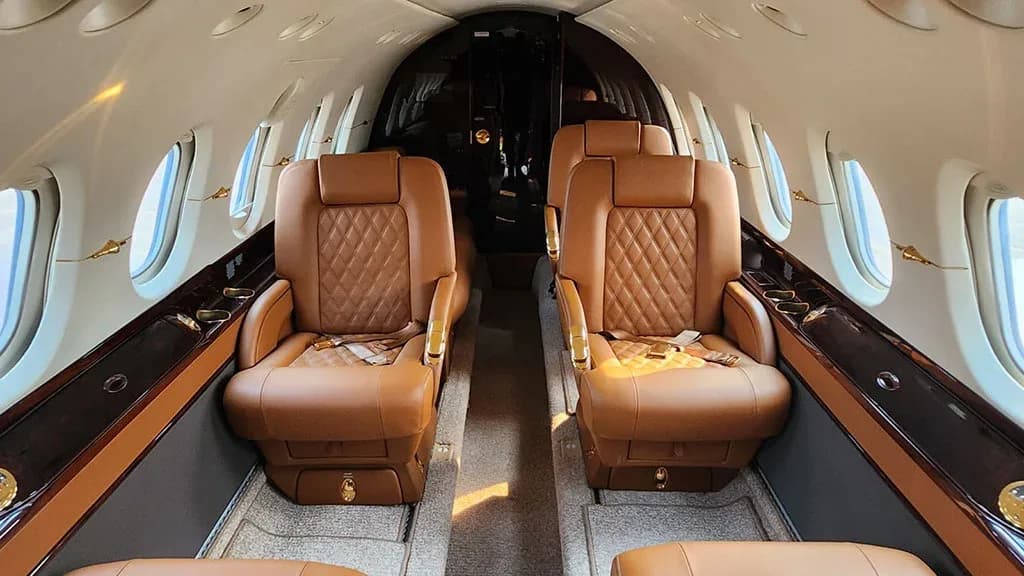 The luxurious interior cabin of a business jet with two rows of quilted brown leather seats facing each other.