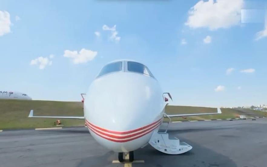 A head-on view of a white business jet with red stripes, parked on an tarmac with its main door open.