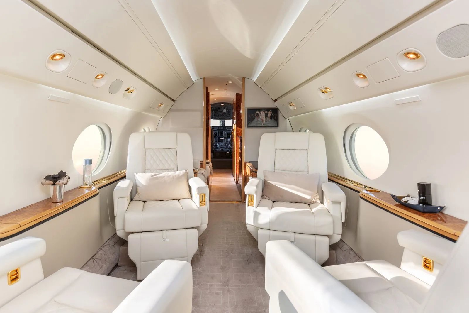 A view down the aisle of a luxurious aircraft cabin with white leather seats and wood accents.