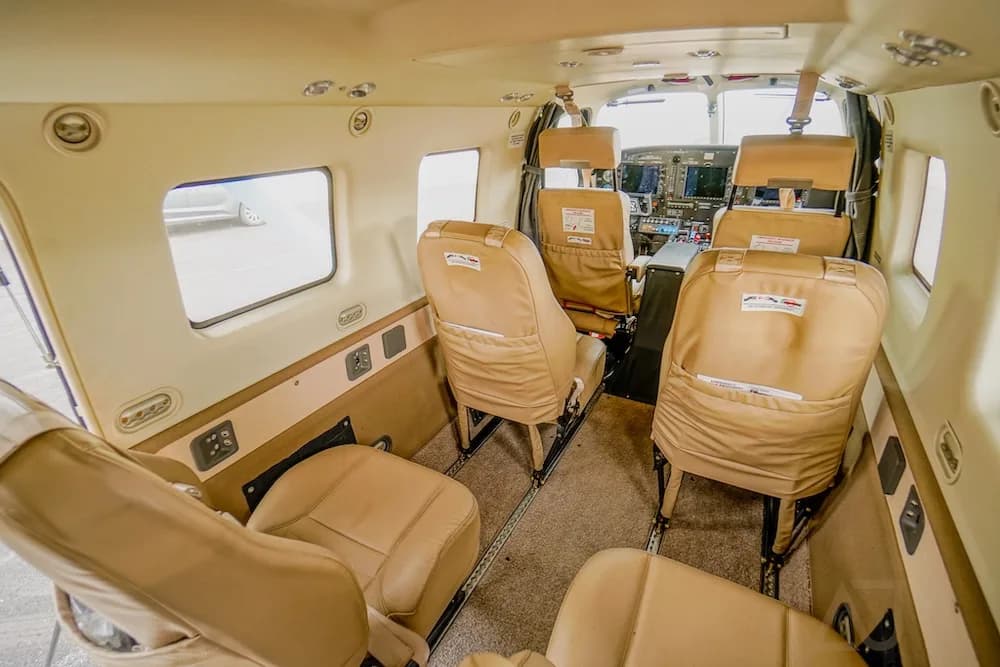 A view of the aircraft interior cabin with tan seats and a partial view of the cockpit instruments.