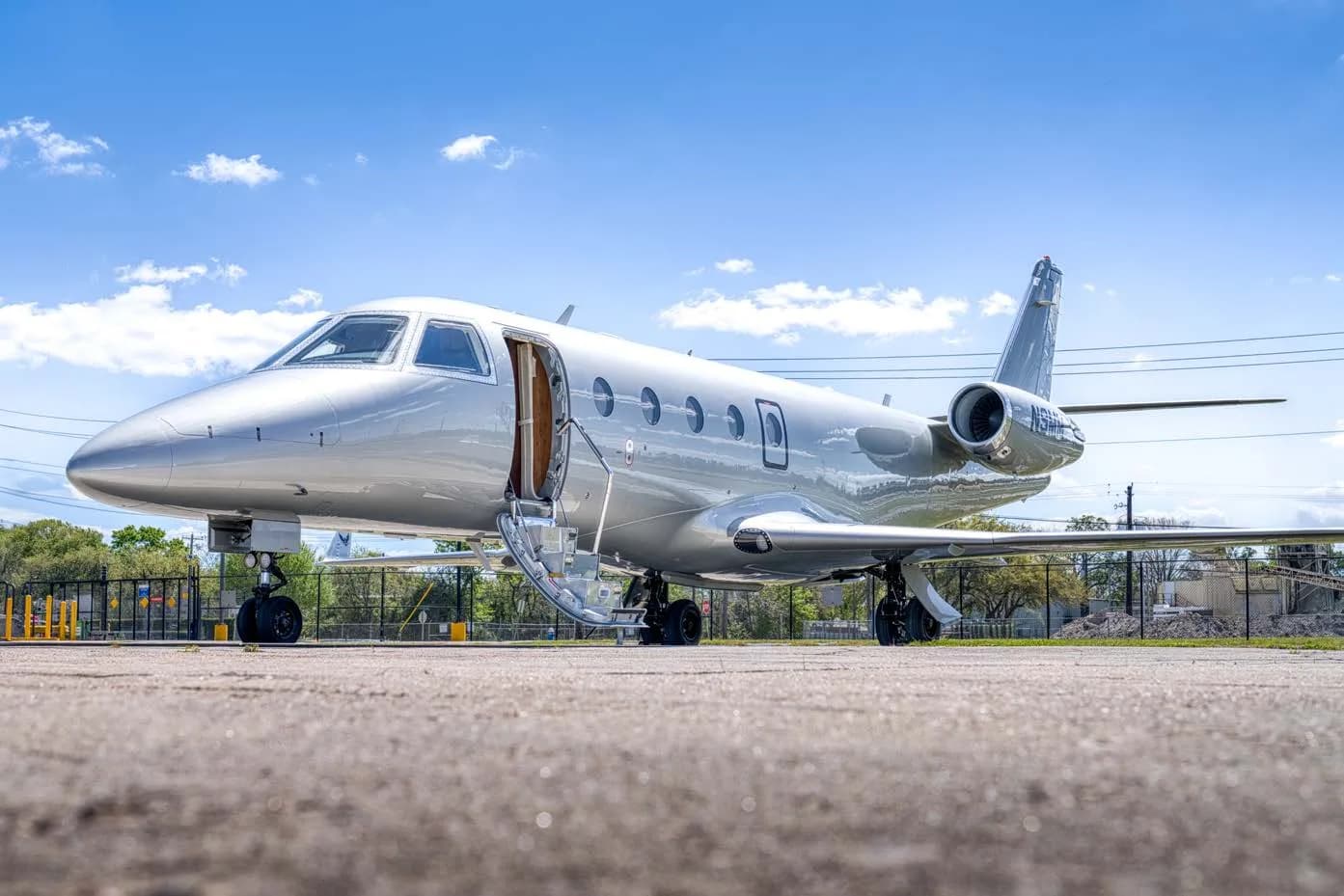 A low-angle view of a silver business jet with its main cabin door open on an airfield.
