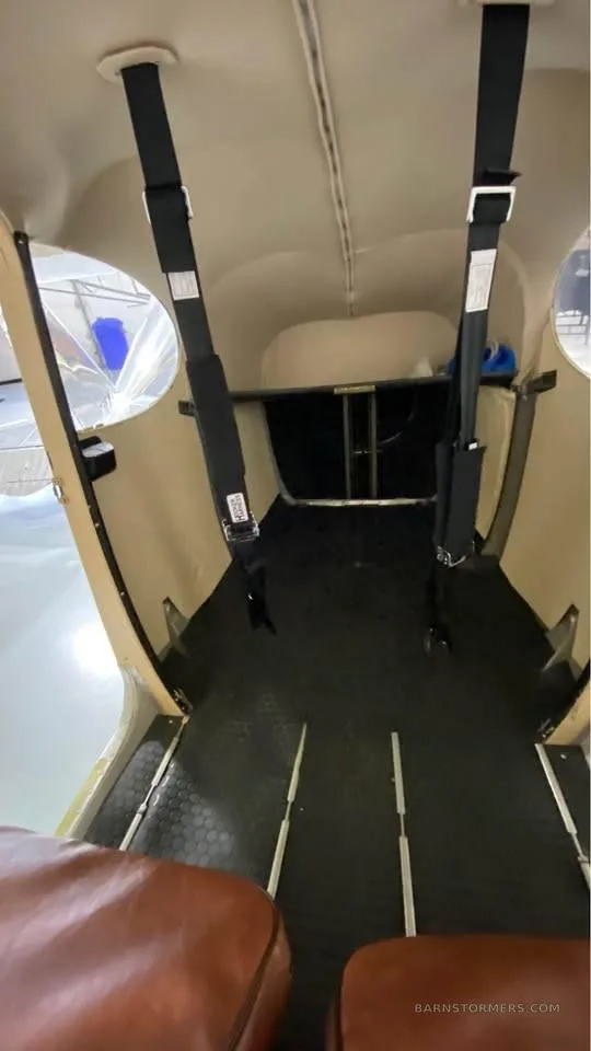 View of the aircraft's rear cabin interior with black seatbelts hanging and a beige headliner.
