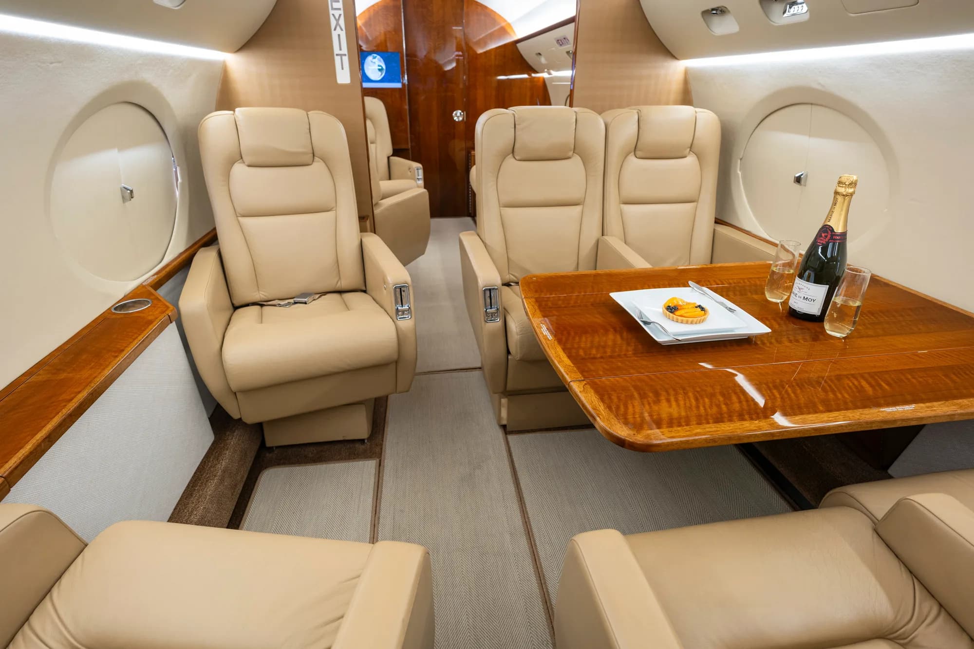A private jet cabin interior showing beige leather seats and a polished wooden dining table.