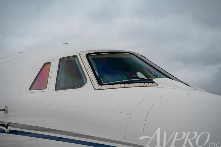 A close-up view of the cockpit windows of the white Cessna Citation Sovereign, showing iridescent reflections.