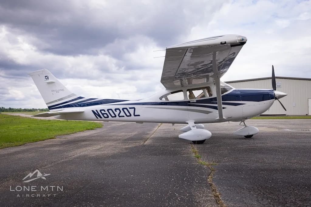 A left-side view of a white and blue Cessna Skylane TC (N6020Z) with flaps extended, parked on an airfield.