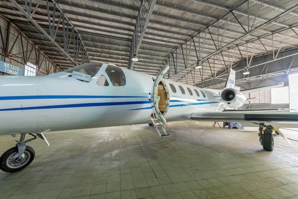 A white Cessna Citation II aircraft with blue stripes is parked in a hangar with its door open.