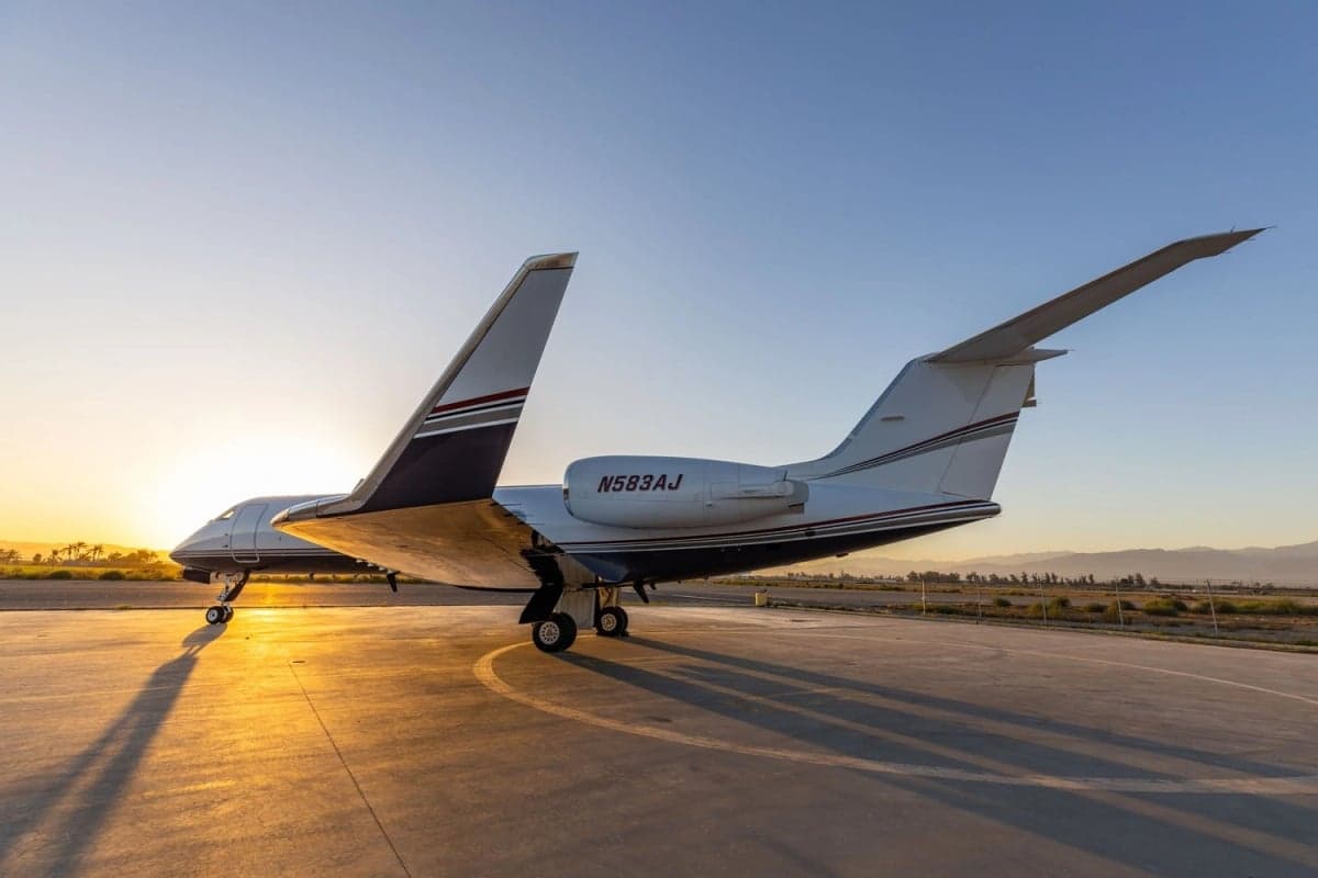 Rear quarter view of a white and brown Challenger 300 on the tarmac at sunset.
