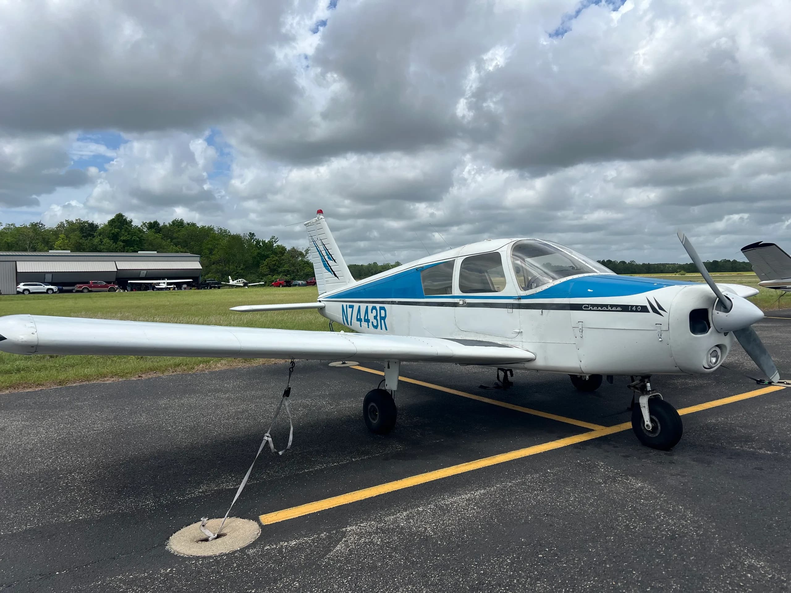 Side view of a white and blue Piper Cherokee 140 (N7443R) parked on an asphalt ramp.