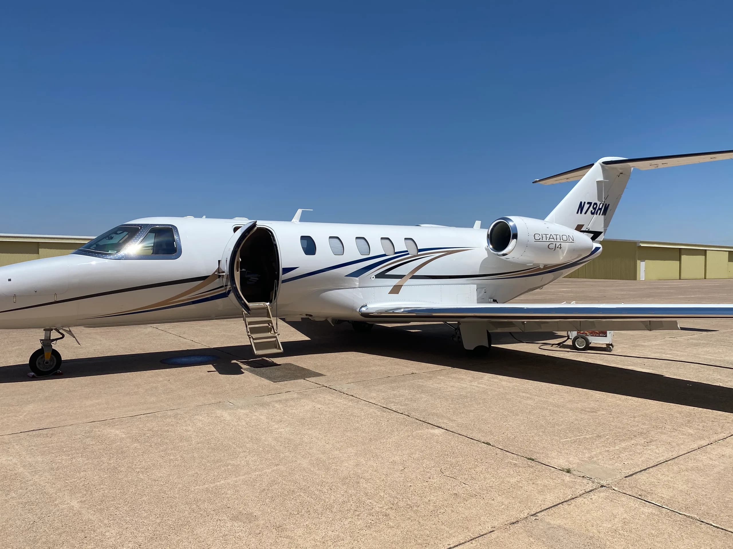 A white business jet with blue stripes, tail number N737J, parked on a tarmac with its door open.