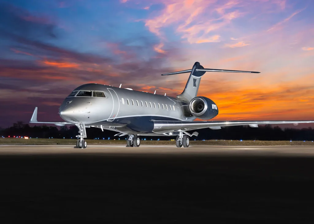A silver and blue Bombardier Challenger sits on the tarmac at sunset.
