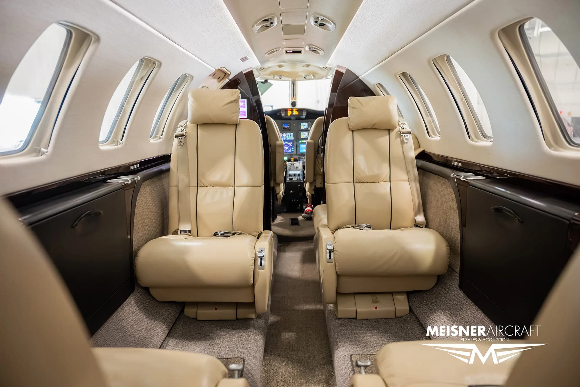 The interior cabin of a business jet, featuring two rows of beige leather seats facing forward.