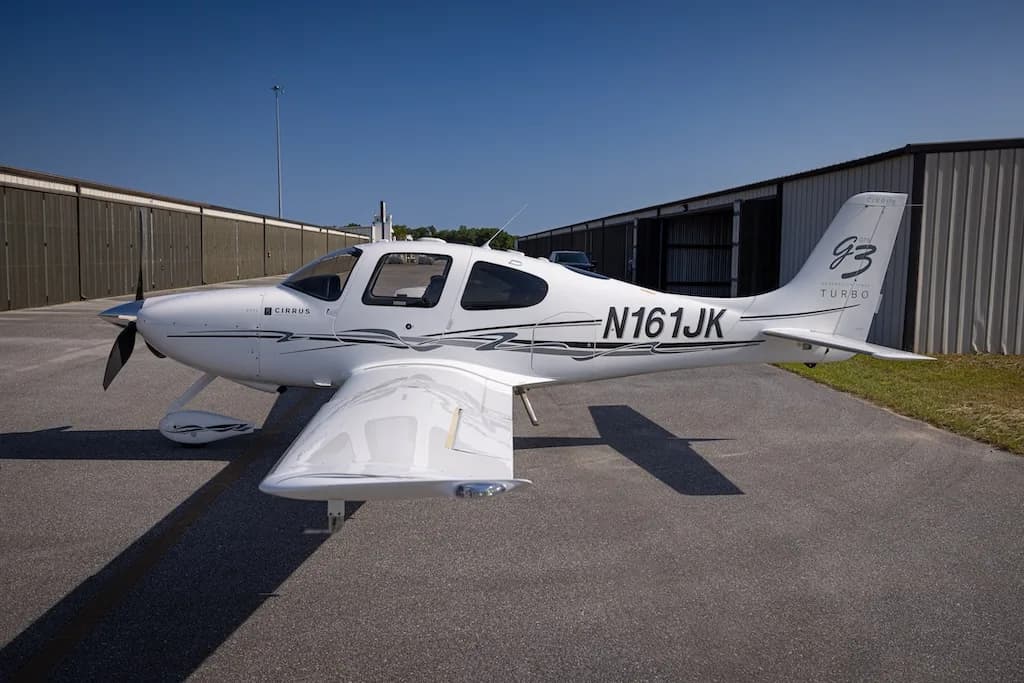 A white Cirrus SR22 G3 Turbo aircraft, registration N161JK, parked on an asphalt tarmac with hangars in the background.