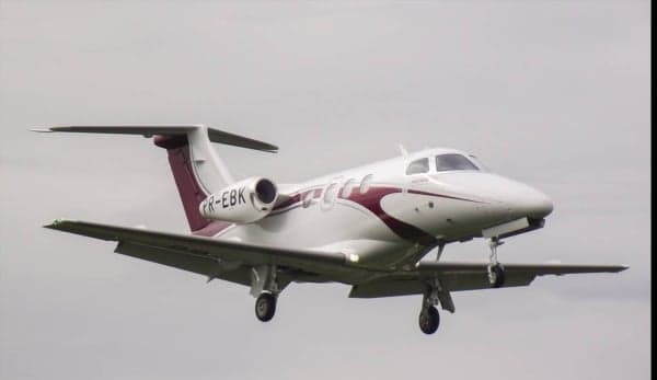 A white and maroon Embraer Phenom 100 is shown in flight.