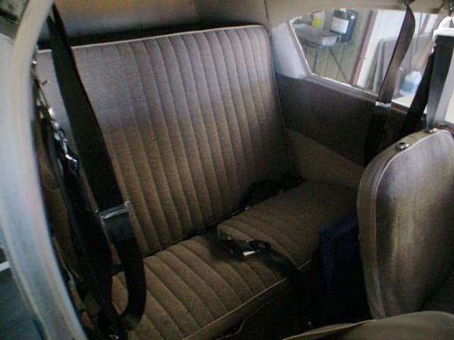 The brown fabric rear bench seat with seatbelts in the interior of a small aircraft.