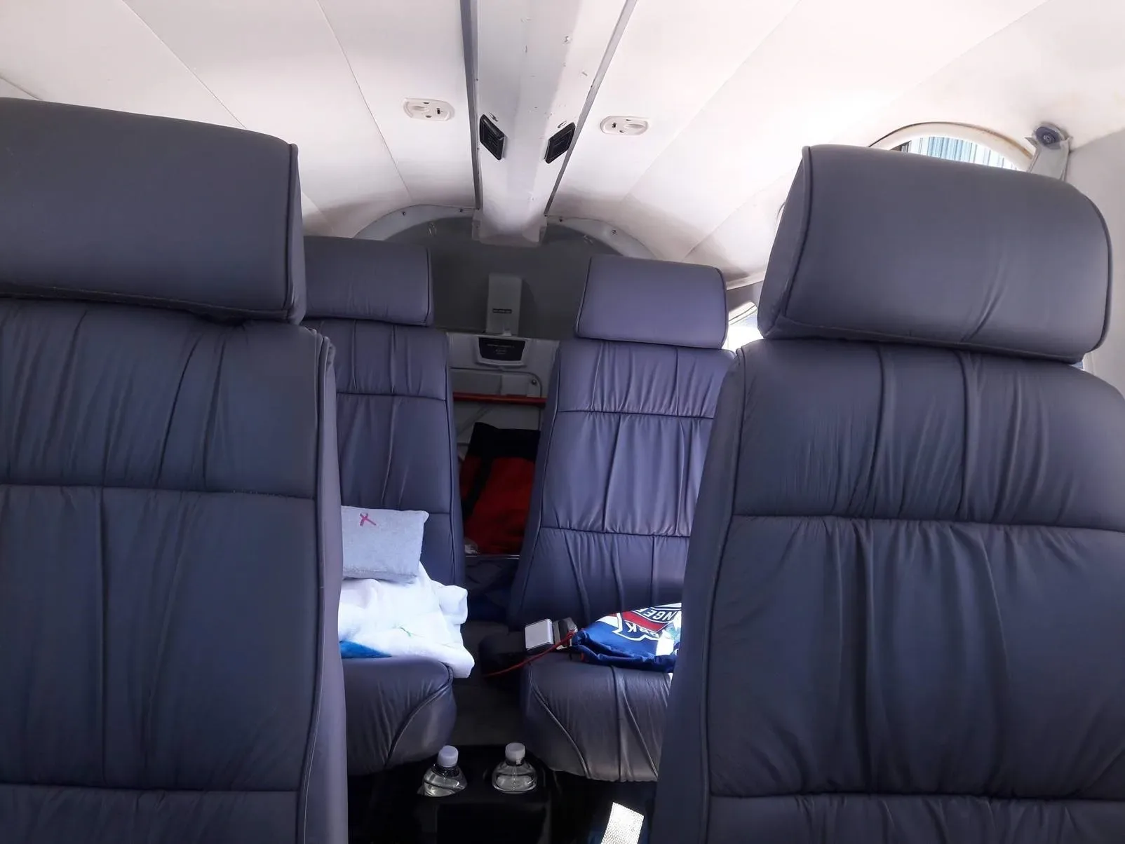 The aircraft cabin interior with four dark grey leather seats and a light-colored ceiling.