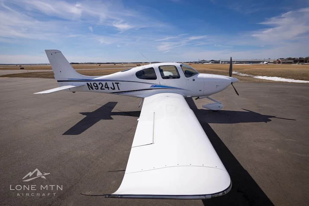 An overhead view of a white single-engine aircraft with blue and black stripes, tail number N924JT, parked on an airport tarmac.
